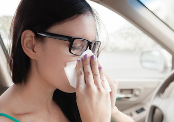 Flu cold or allergy symptom. Sick woman girl sneezing in tissue while in her car.