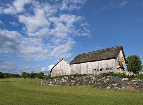 Pair of Old Wooden Barns: Timber frame barns weathered white in color sitting on a bluff with a blue sky and white clouds in New York's Hudson Valley