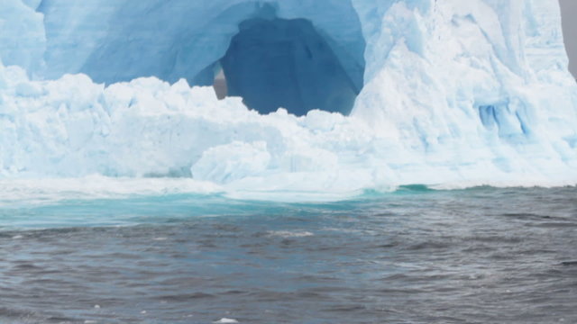 Close up of waves in arches of large tabular iceberg in rough seas of Drake Passage near Antarctica on stormy day.
