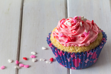 Single Vanilla Cupcake with Pink Buttercream Frosting and Heart Sprinkles on a Wooden Table with Copy Space from Above