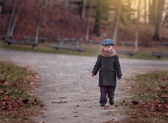 Fototapeta premium serious little boy wearing a hat walking on a path in a park on a chilly day