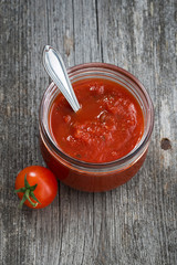 tomato sauce in a glass jar on a wooden background, top view