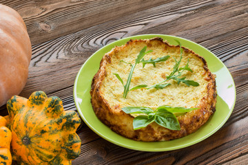 casserole from squash decorated by basil leaf and arugula on light green plate on wooden table with squash fruits  and pumpkin