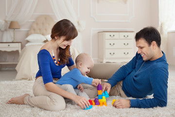 Obraz na płótnie Canvas Young parents and cute son play building kit sitting on a carpet in children room