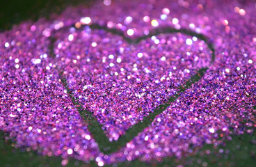 Blurry abstract background with heart of purple glitter on black surface