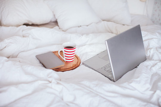 open laptop with a cup of tea and a book lying on a white bed