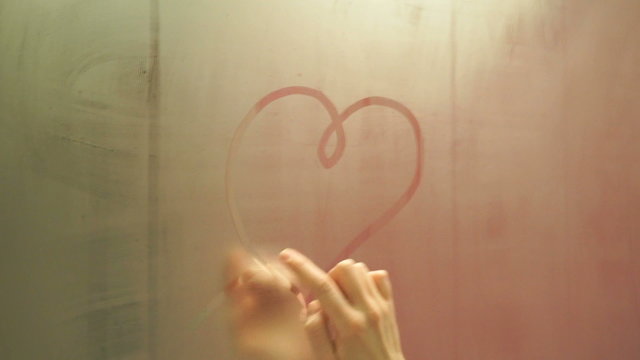 the girl draws a finger drawing a heart on a foggy mirror fast