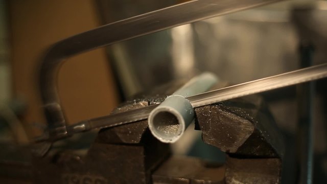 Man sawing with a manual hacksaw the pipe, gripped in a vise installed on the workbench
