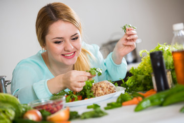 Young woman decorating salad with herbs in kitchen