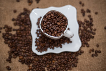 Fototapeta na wymiar a scattering of coffee beans white cup and saucer on a table brown texture units large lot of grain
