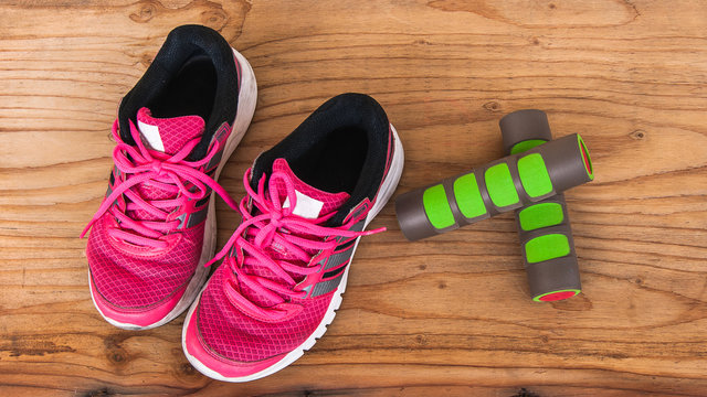 Old pink sneakers with fitness dumbbells on wood background