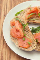 bread with smoked salmon on white plate on brown wooden background