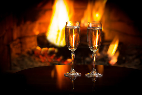 Two glasses of sparkling white wine in front of warm fireplace. Romantic, cozy relaxed magical atmosphere near fire. Valentines day concept. Background