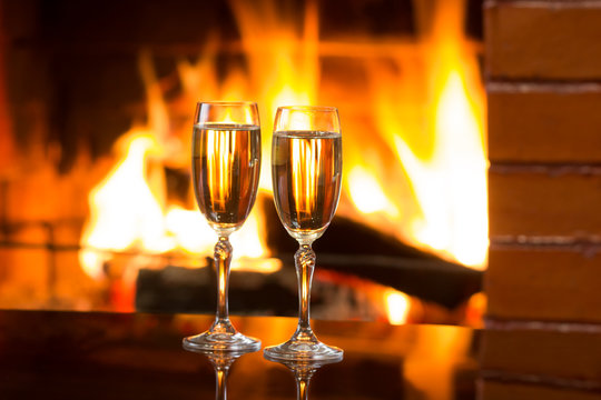 Two glasses of sparkling white wine in front of warm fireplace. Romantic, cozy relaxed magical atmosphere near fire. Valentines day concept