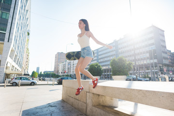 Fototapeta premium Young beautiful asiatic woman skater jumping from a wall, listen