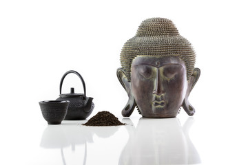 Isolated Buddha head, iron teapot, iron cup and tea on a white background and lotus with reflection
