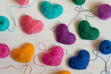 Multicolored Hearts with a balls of thread on white wooden backg