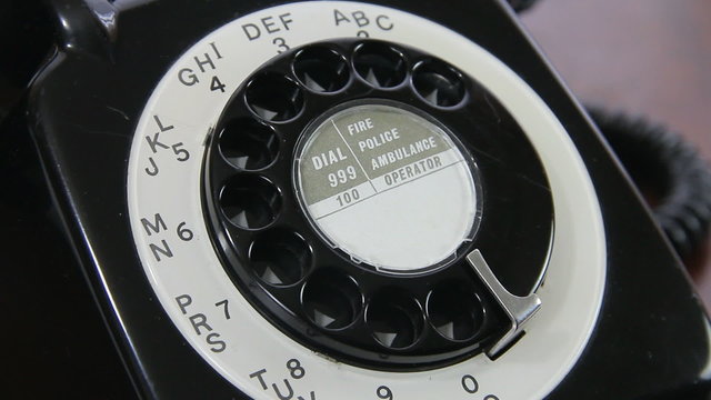 Close up of a man's hand dialling a number on a mid 20th century UK rotary dial telephone.  A six digit number is dialled.