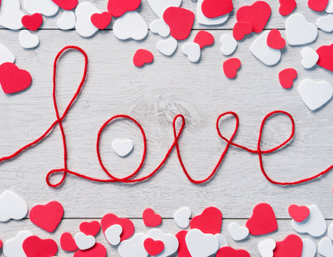 Word "love" with heap of small hearts on wooden background. View from above.