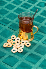 Glass cup of tea in an aluminum cup holder with fragrant green bagels on tablecloth