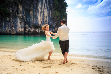 groom blonde bride in fluffy dress join hands swing on beach