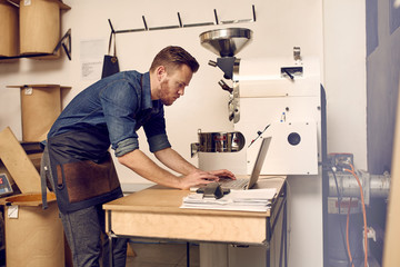 Modern coffee roaster using his laptop alongside a modern roasti