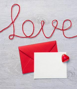 Word "love" and red envelope with letter on wooden background. View from above. Valentines Day concept