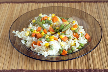 China white rise with vegetables in translucent plate on brown wicker straw mat front view closeup