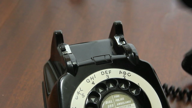 Close up of a man's hand picking up and replacing the handset on mid 20th century UK rotary dial telephone.