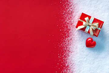 Holiday gift and red heart in the snow with red paper background. Copy space for your text. St....