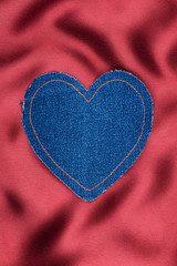 Heart made of denim fabric with yellow stitching on red silk