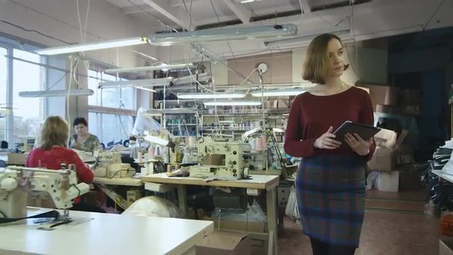 Young brunette with a tablet is walking through a clothing factory. Shot on RED Cinema Camera.