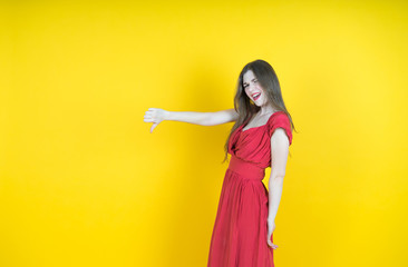 beautiful long-haired   girl showing thumbs down,   photo studio, portrait of a woman isolated on yellow background