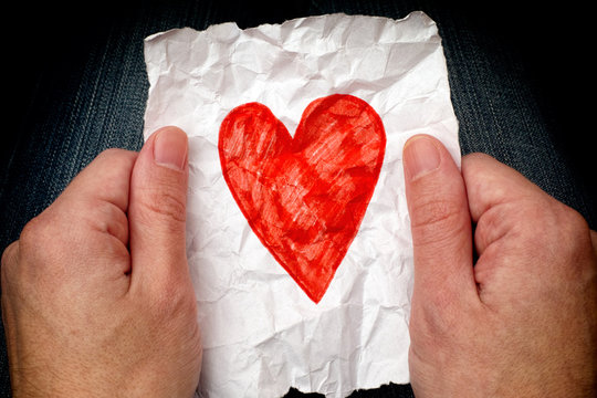 Young man holding crumpled piece of paper with red heart