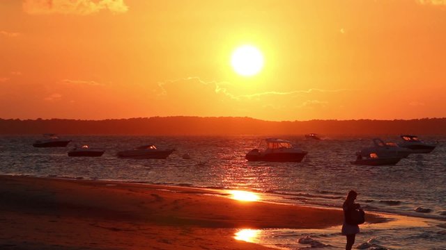 Woman taking a picture of sunset on the beach, France - Full HD. Woman taking a picture of the sunset at the beach. A boat crossing the horizon - France