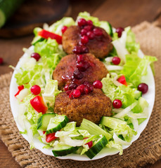 Juicy meat cutlets with cranberry sauce and salad on a wooden table in a rustic style.