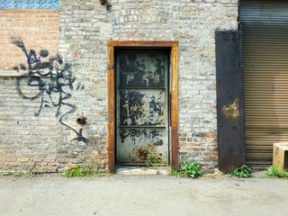 Fototapeta na wymiar Doorway on brick wall in urban setting with graffiti - landscape photo