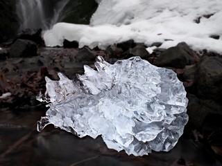 Beautiful big piece of ice with abstract cracks. Icicle bellow waterfall, stony and messy stream bank