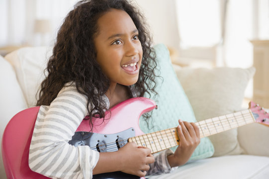 Mixed race girl playing electric guitar on sofa