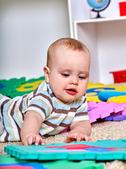 Portrait of kid baby boy lying on floor and plying with puzzle toy. 