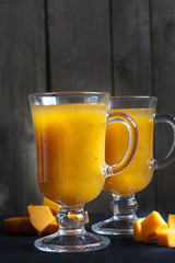 Fresh pumpkin juice in tall glass, pieces of fresh pumpkin on the black desk
