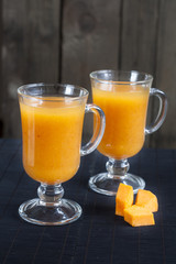 Fresh pumpkin juice in tall glass, pieces of fresh pumpkin on the black desk