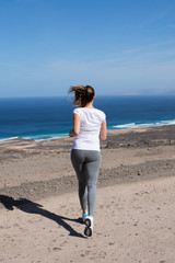 Rear view of woman running in the mountains with beach in front
