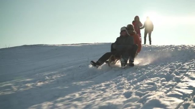 4k footage, happy best agers on sunny winter day out in snow, woman pushing senior men on toboggan
