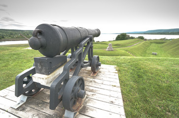 Old guns of yester year, a cannon overlooking lands they once defended, from the 18th century, sits on its display platform, never to fire again.  Spring day in Nova Scotia.