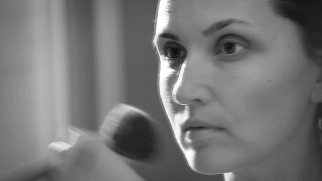 Black and white footage: young woman applies makeup