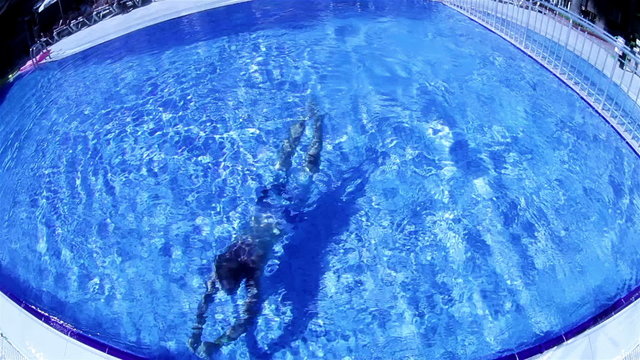 Man is crossing the round pool swimming under the water