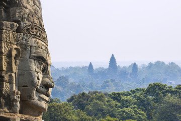Naklejki  Starożytna kamienna twarz ze świątynią Angkor Wat w dżungli na tle