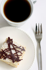 isolated slice of decorated with chocolate napoleon cake and black coffee, served on white plate