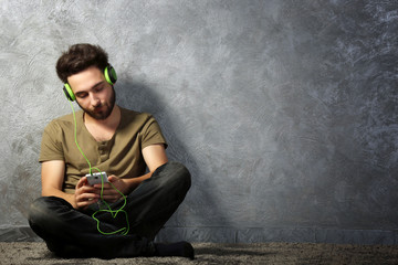 Young bearded man listens music with headphones sitting on grey wall background